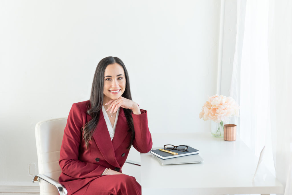 business woman in red pant suit sitting at a white desk for a brand photoshoot
